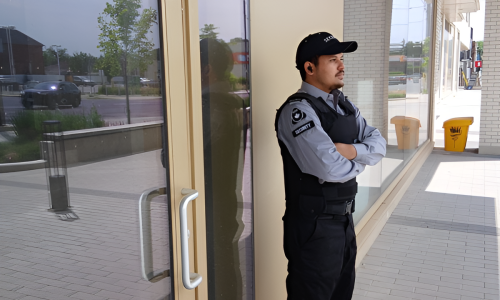 Uniformed Nicagon guard on access-control duty at a commercial building's glass entrance